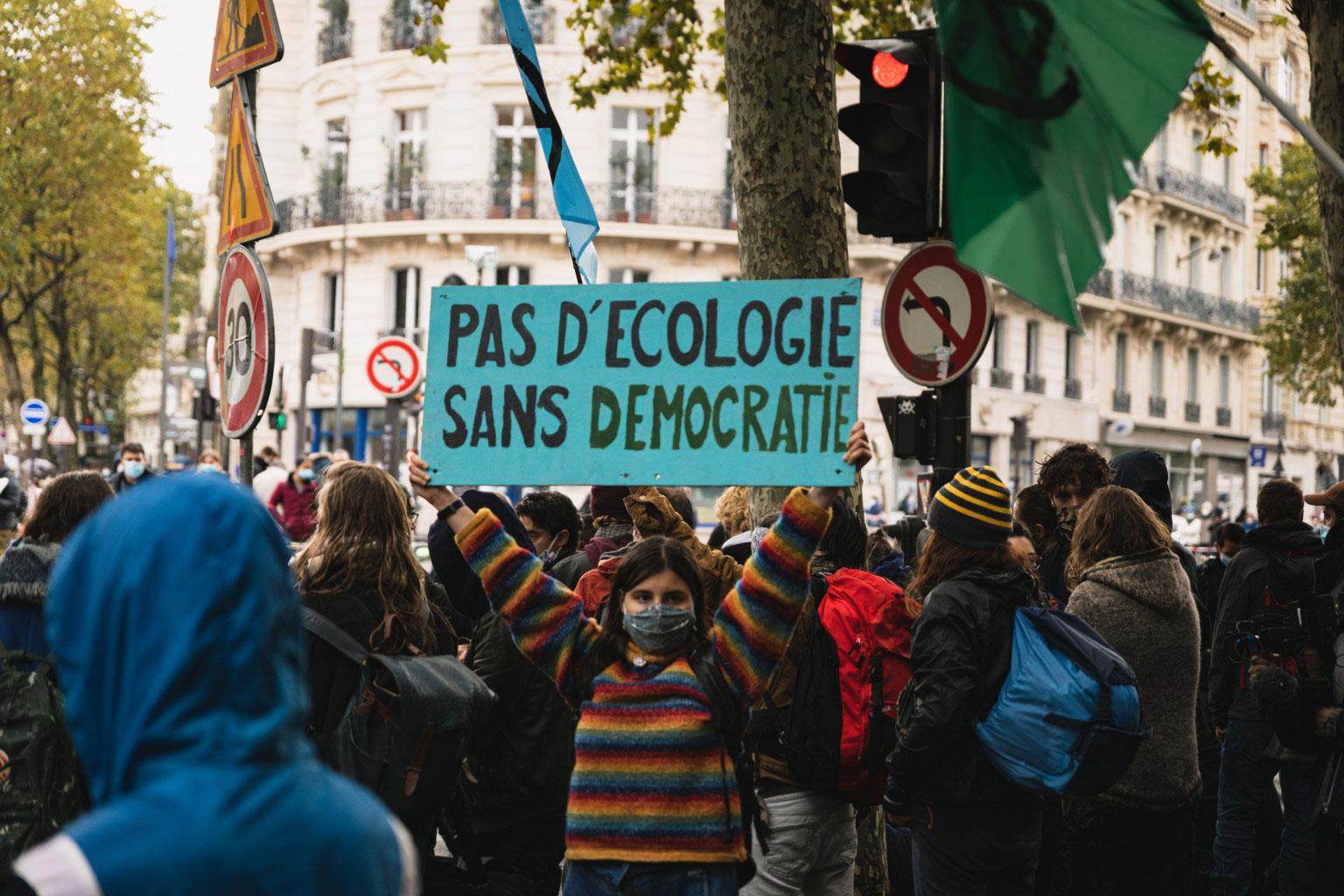 Rebelle portant une pancarte « Pas d'écologie sans démocratie »
